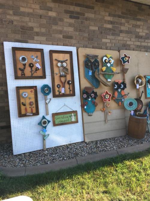 A display of colorful garden art made from various materials, featuring owls and flowers on wooden boards.