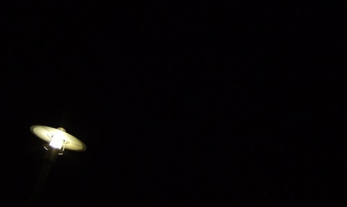 A dimly lit streetlamp against a dark night sky.