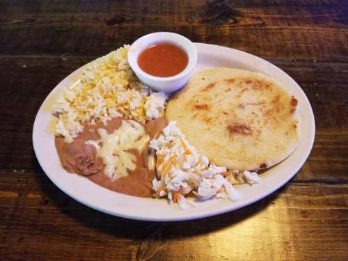 A plate of rice, refried beans, coleslaw, a tortilla, and a small bowl of salsa on a wooden table.