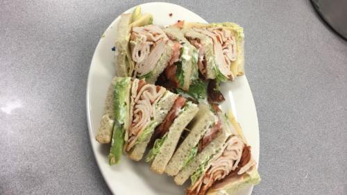 A plate of sliced turkey sandwiches with lettuce, bacon, and mayonnaise on white bread.