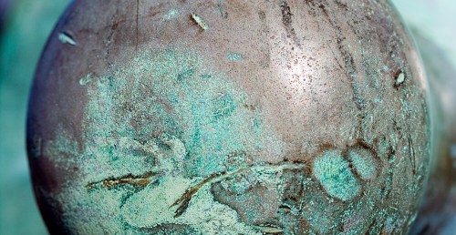 Close-up of a textured, weathered metal surface with green patina and subtle details.