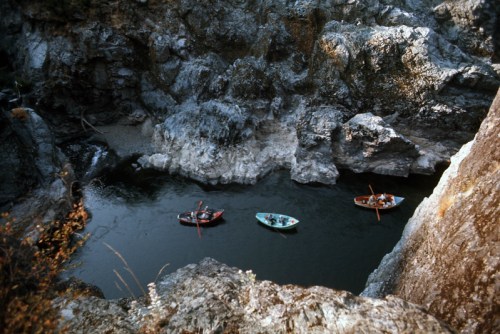 Three small boats navigate a winding river surrounded by rocky cliffs and sparse vegetation.