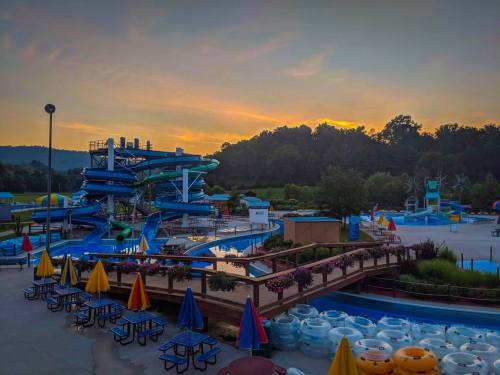 A water park at sunset, featuring colorful slides, pools, and lounge areas with umbrellas and inner tubes.