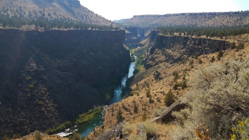 A scenic view of a winding river cutting through a rugged canyon surrounded by dry hills and sparse vegetation.
