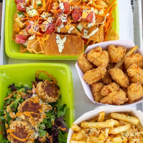 A vibrant spread of nachos, salad, popcorn chicken, and fries in colorful containers on a tray.