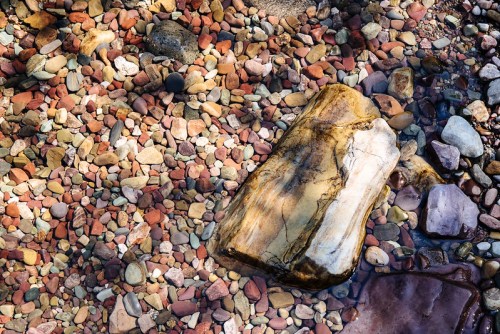 A variety of colorful pebbles and a large stone partially submerged in clear water.