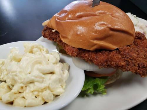 A crispy fried chicken sandwich on a bun, served with a side of creamy macaroni salad.
