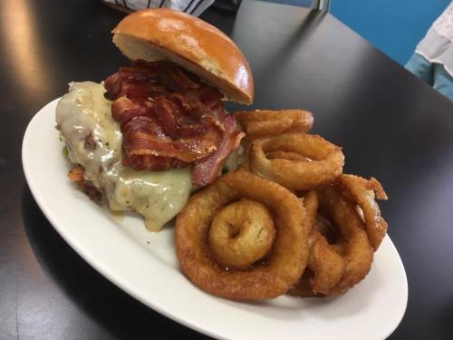 A juicy burger topped with melted cheese and crispy bacon, served with a side of golden onion rings on a white plate.