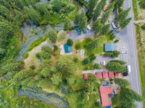 Aerial view of a green landscape with trees, a river, and a small cluster of buildings near a road.