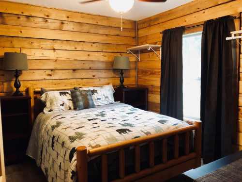 Cozy bedroom with wooden walls, a double bed, two lamps, and a window with dark curtains.