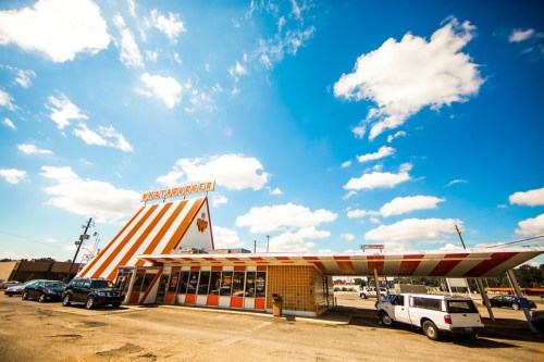 A colorful fast-food restaurant with a distinctive triangular roof and orange and white stripes under a blue sky.