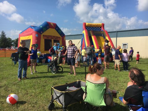 A lively outdoor scene with families enjoying inflatable bounce houses and beach balls on a sunny day.