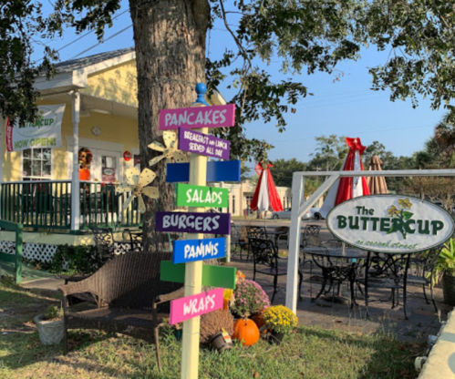 A colorful signpost outside The Buttercup restaurant, listing menu items like pancakes, salads, and burgers.