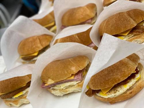 A close-up of several breakfast sandwiches on a tray, each wrapped in white paper, featuring layers of egg, cheese, and meat.