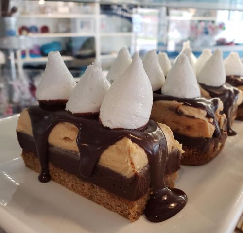 A close-up of a dessert featuring layers of chocolate and peanut butter, topped with whipped cream peaks.