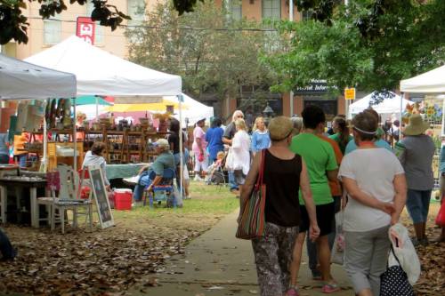 A bustling outdoor market scene with people walking among vendor tents and colorful displays.