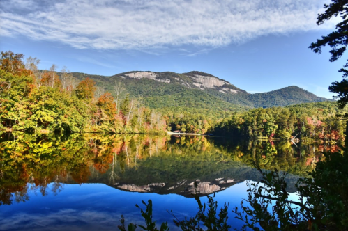 A serene lake reflects colorful autumn trees and mountains under a clear blue sky.