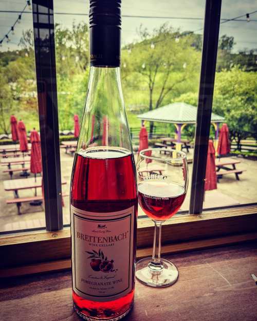 A bottle of Breitenbach pomegranate wine next to a glass, with a scenic outdoor patio visible through the window.