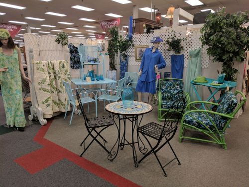 A cozy display featuring colorful outdoor furniture, decorative plants, and stylish clothing in a retail setting.