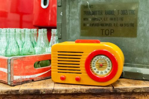 A vintage yellow radio with a round dial, placed next to glass bottles and a wooden crate.