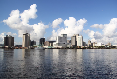 City skyline reflecting on water under a blue sky with fluffy clouds.