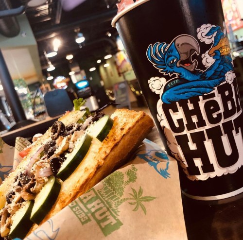 A sandwich with cucumbers and toppings next to a colorful drink cup at a restaurant.