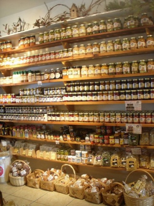 A well-stocked shelf displaying various jars of preserves, sauces, and packaged goods in a cozy store.