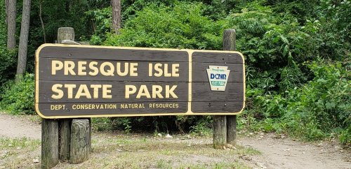 Sign for Presque Isle State Park, surrounded by greenery, indicating it's managed by the Department of Conservation and Natural Resources.