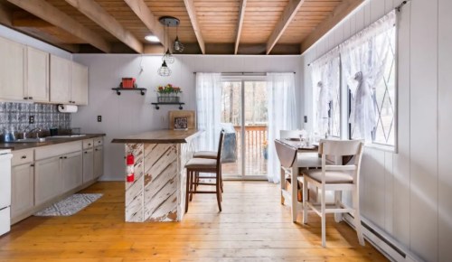 Cozy kitchen with wooden beams, light cabinets, a bar area, and large windows overlooking a deck.