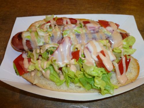 A hot dog in a bun topped with lettuce, tomatoes, and drizzled with sauce.