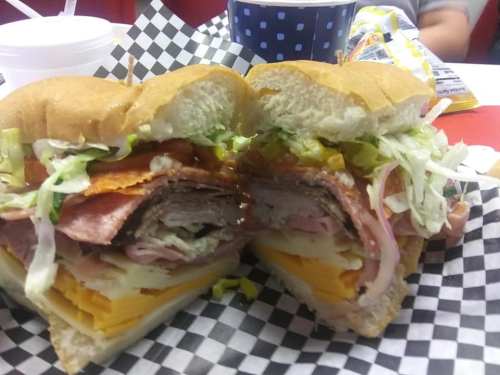 A large sandwich cut in half, filled with various meats, cheese, lettuce, and toppings, served on a checkered paper.