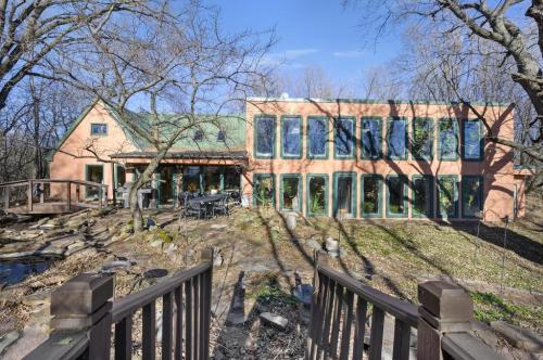 A modern house with large windows, surrounded by trees and a stone pathway leading to a small pond.