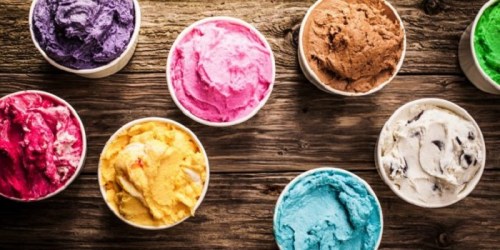 Colorful ice cream scoops in cups arranged on a rustic wooden surface.