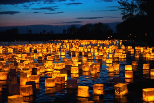 A serene lake at dusk filled with glowing lanterns, casting warm reflections on the water's surface.