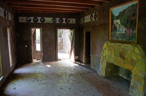 Interior of an abandoned room with a stone fireplace, graffiti on the walls, and two open doors leading outside.
