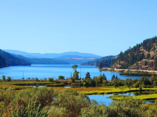 A serene lake surrounded by lush greenery and mountains under a clear blue sky.