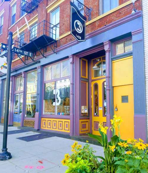 Colorful storefront with purple and yellow accents, large windows, and yellow flowers in front.
