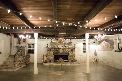 Cozy indoor space with a stone fireplace, wooden beams, and string lights, creating a warm, inviting atmosphere.
