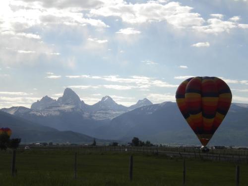 A colorful hot air balloon floats near mountains under a cloudy sky, with green fields in the foreground.