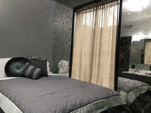 A modern bedroom featuring a bed with gray bedding, decorative pillows, and a curtain separating the space.
