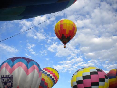 Colorful hot air balloons against a blue sky with fluffy clouds, some balloons in the foreground and one soaring above.