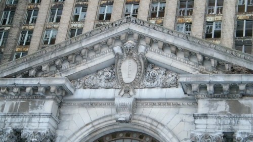 Close-up of ornate architectural details on a weathered building facade, featuring intricate carvings and a decorative shield.