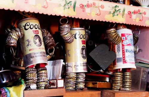 Three whimsical figures made from beer cans and bottle caps, displayed on a shelf among various collectibles.