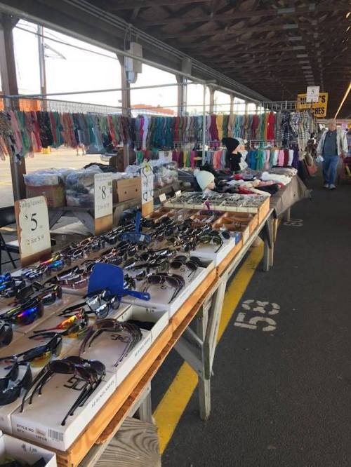 A bustling market stall displaying various sunglasses and colorful accessories under a covered area.