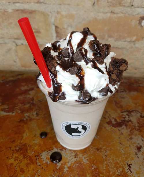 A delicious milkshake topped with whipped cream, chocolate syrup, cookie crumbles, and a red straw.