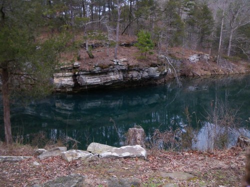 A serene landscape featuring a calm, reflective body of water surrounded by rocky terrain and trees.