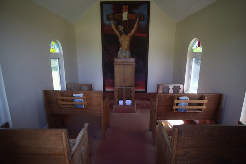 Interior of a small chapel featuring wooden pews, stained glass windows, and a large crucifix on the wall.