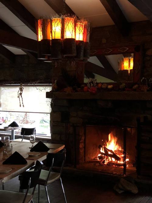 Cozy restaurant interior with a stone fireplace, warm lighting, and a rustic chandelier, creating a welcoming atmosphere.