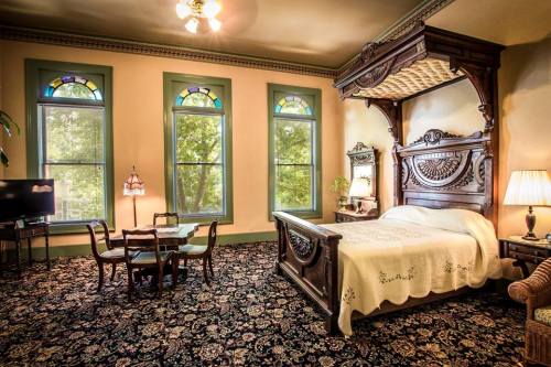 A spacious bedroom with a four-poster bed, vintage decor, a small dining table, and large windows with stained glass.