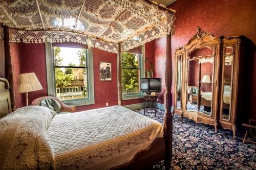 Cozy bedroom with a four-poster bed, vintage decor, a large mirror, and a TV, featuring rich red walls and floral carpet.
